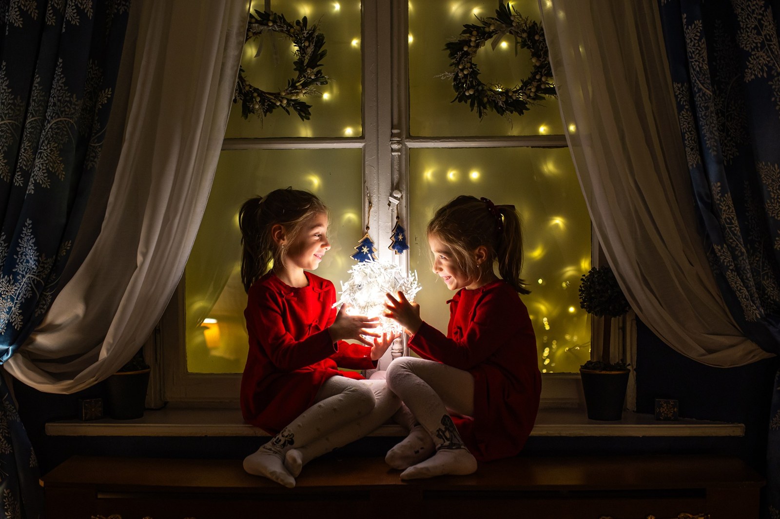 Doua fetite cu o sfera luminoasa la fereastra